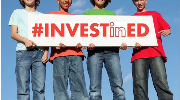 Children holding a sign which reads #investined